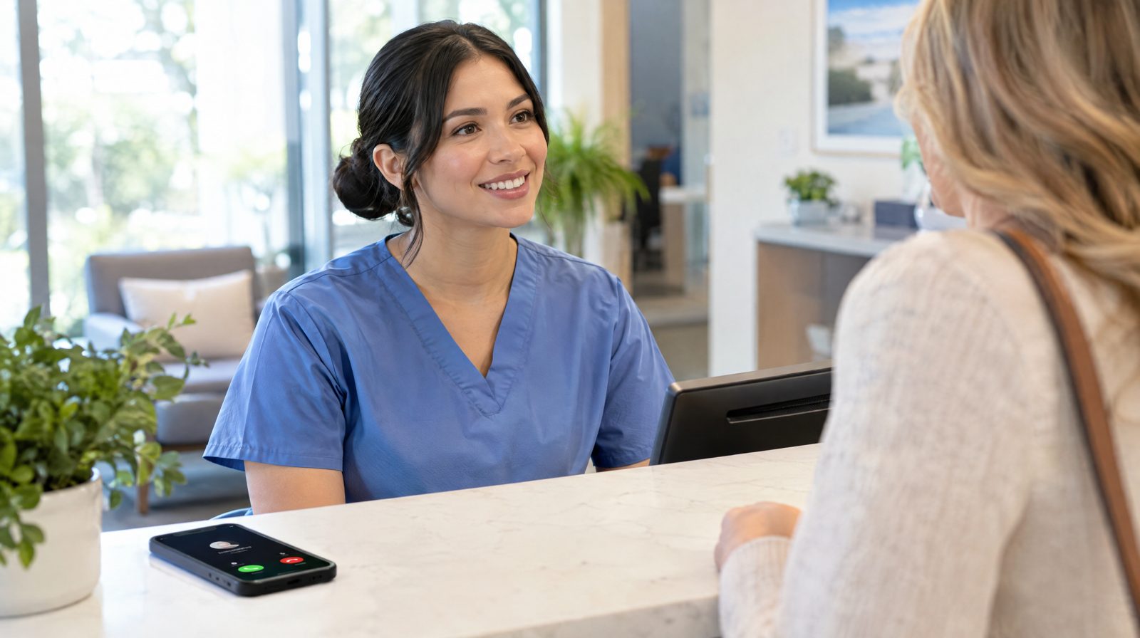 Medizinische Fachangestellte betreut einen Patienten am Empfang, während ein Anruf auf dem Smartphone eingeht